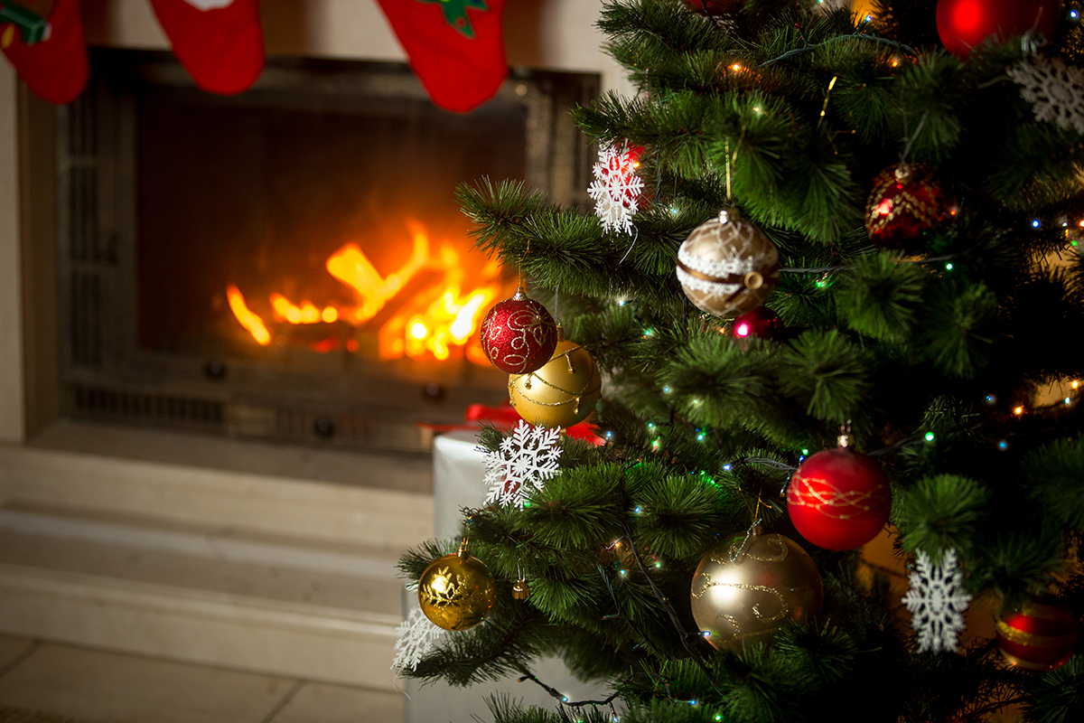 Christmas tree in front of a wood burning stove with decorated fireplace